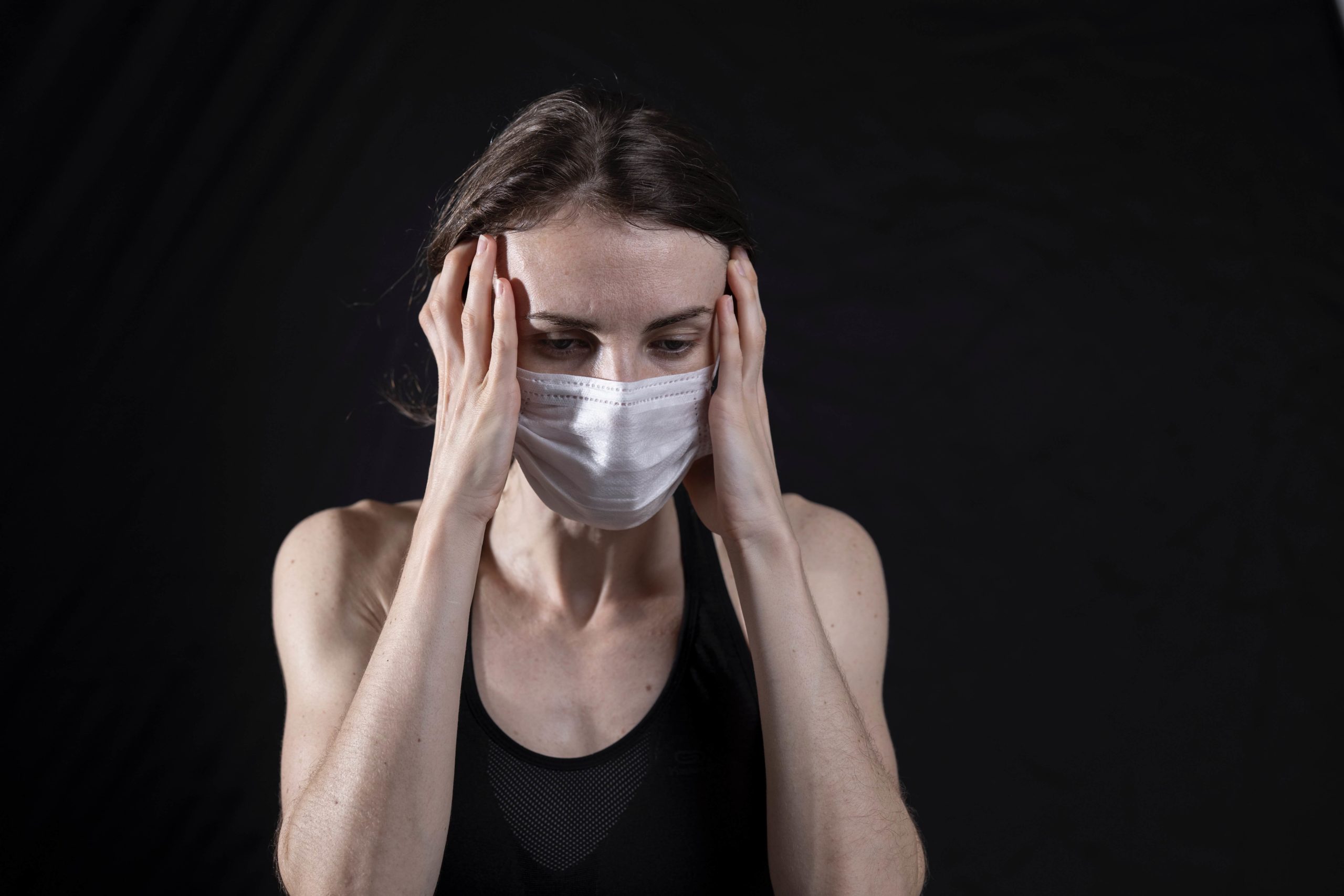woman with a mask on holding her head in stress