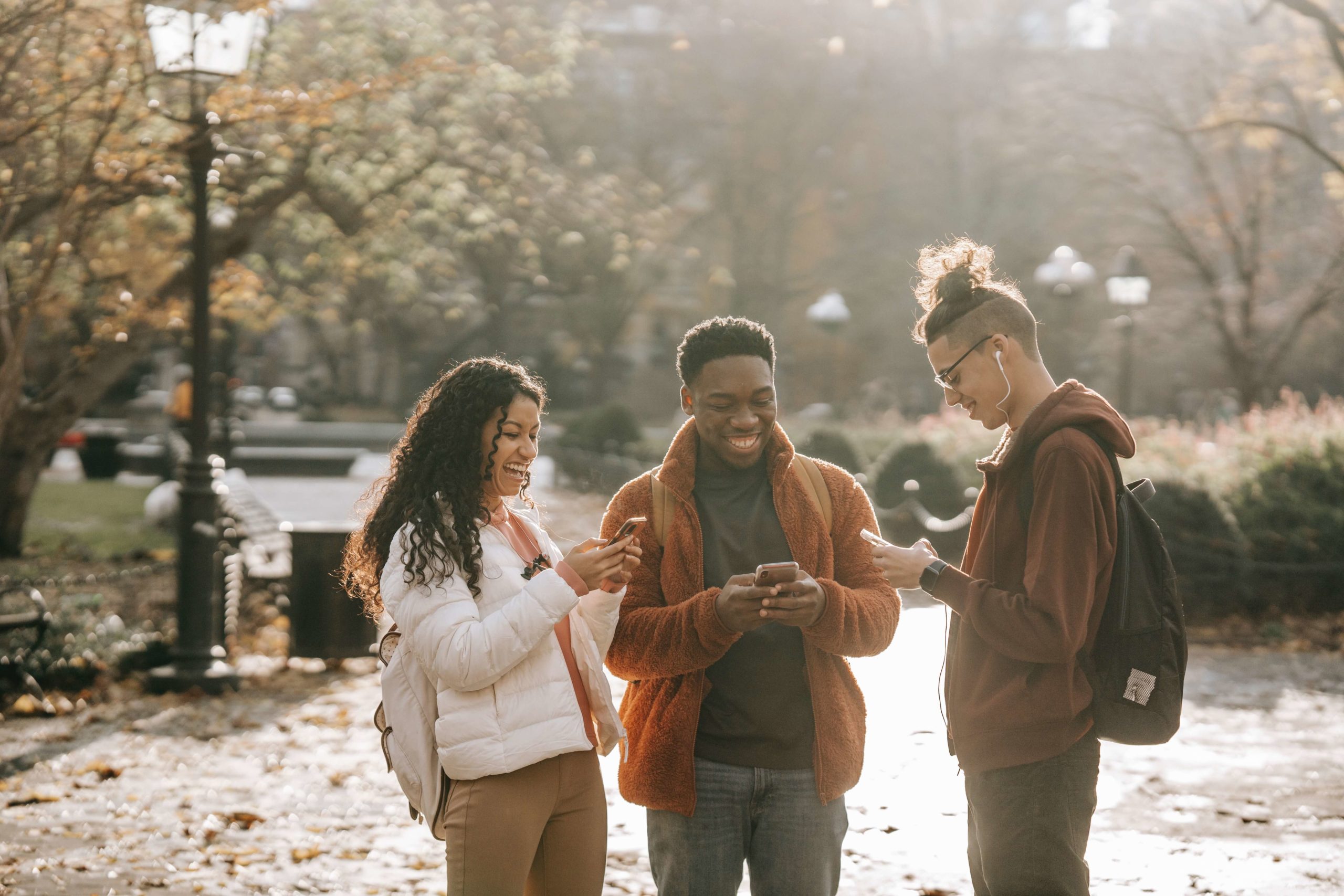 three students standing together, looking at their phones, and laughing